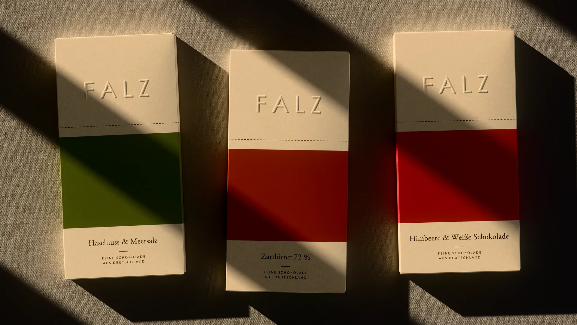 Three FALZ cartons from above on fabric, light stripes across the colour bands