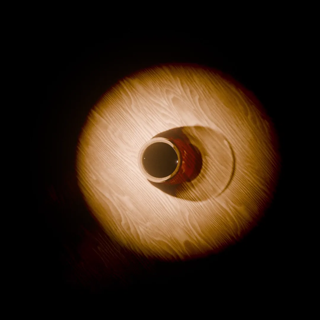 A wine glass seen from above, its shadow and caustics in a pool of light on wood